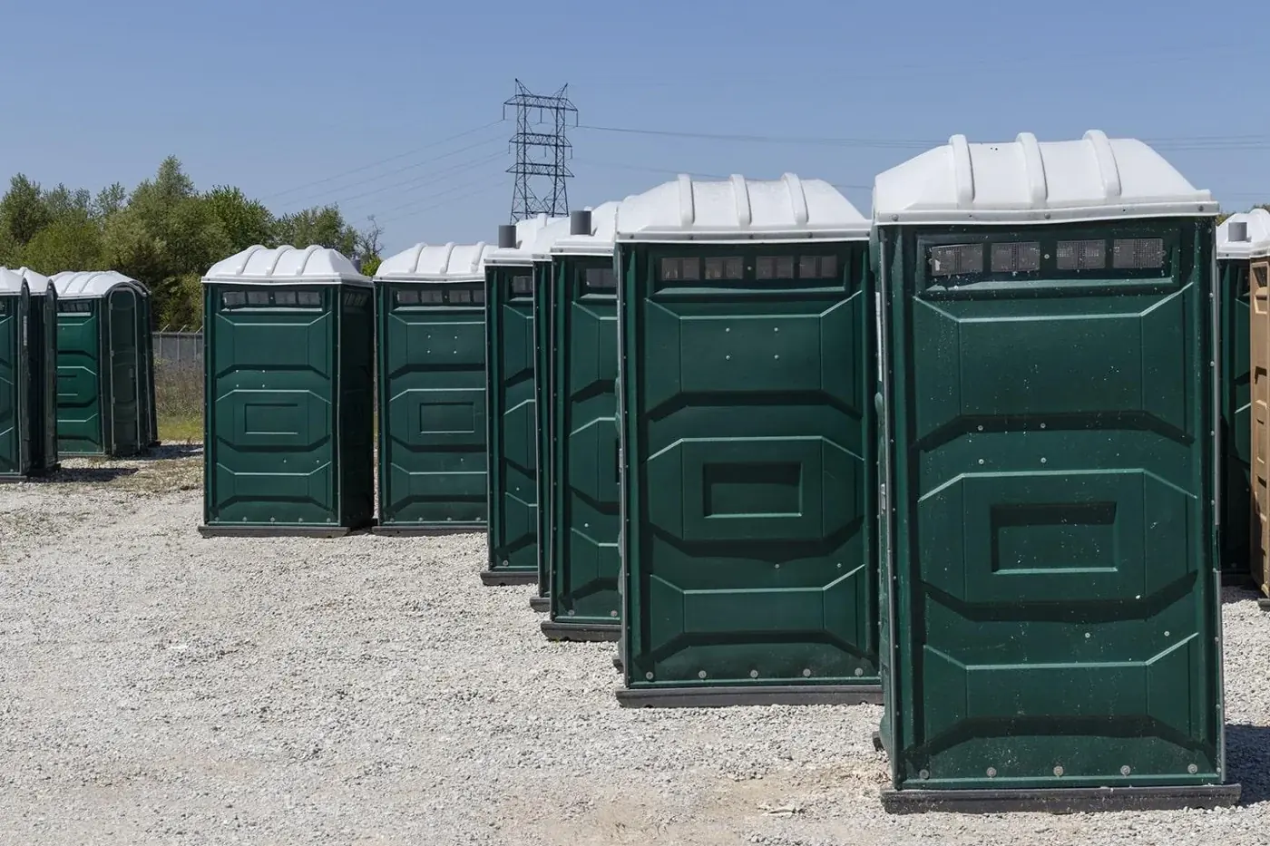 A row of green portable toilets on a gravel surface